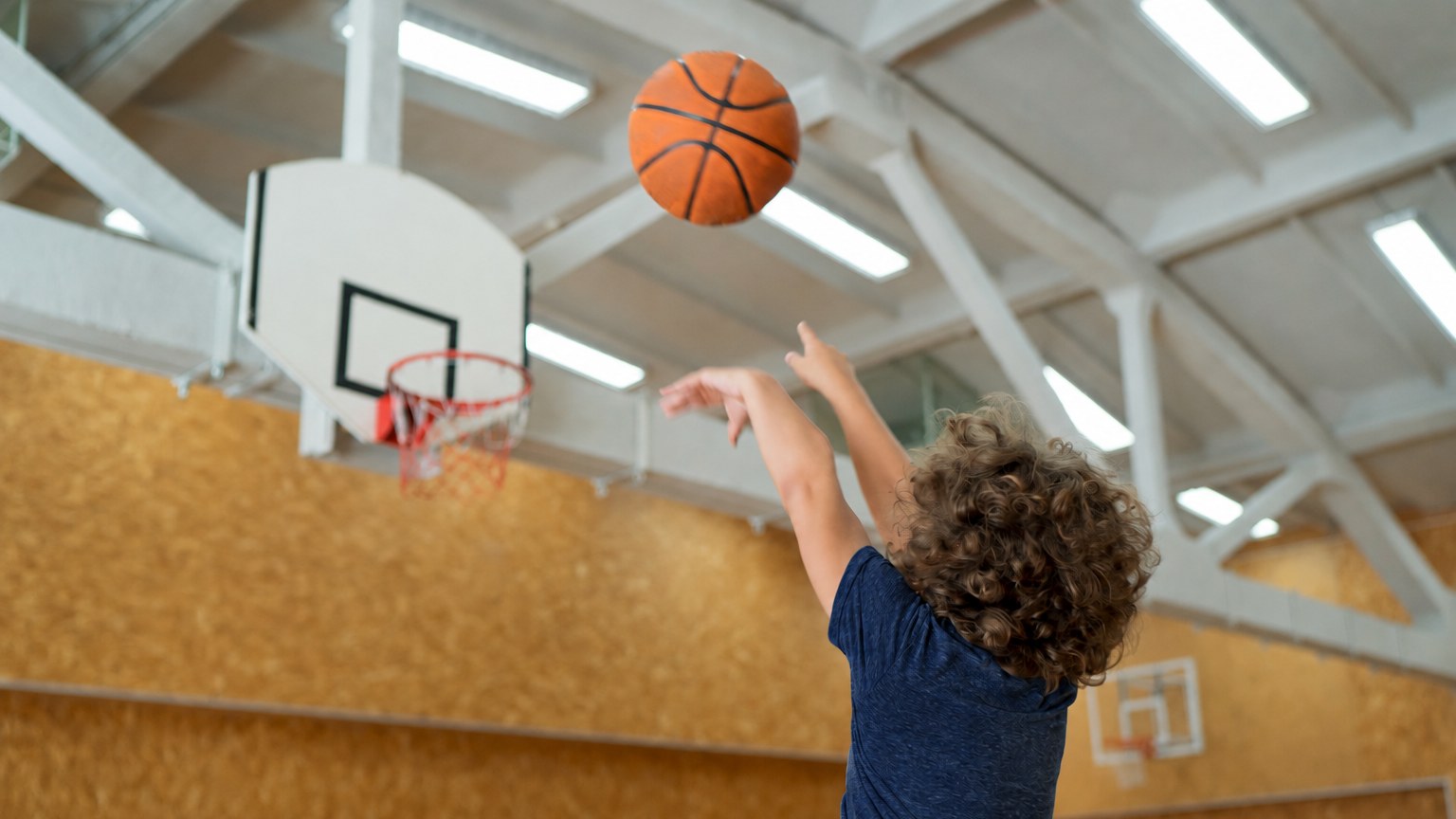 Young boy in a navy Athlantic shirt shooting a basketball toward a hoop in a community gymnasium